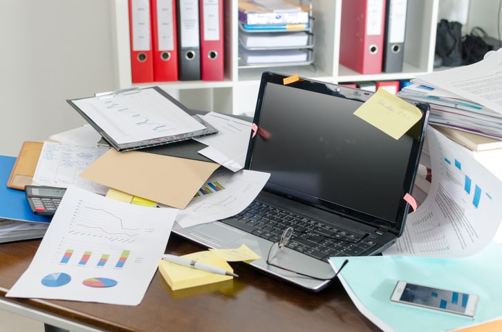 Cluttered office desk with a computer and scattered papers.